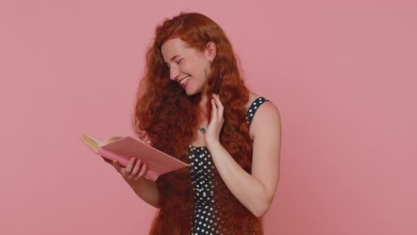 Redhead young woman reading funny interesting fairytale story book, leisure hobby, knowledge wisdom, education, learning, study, wow. Red hair ginger freckles girl isolated on pink studio background - 映像、動画