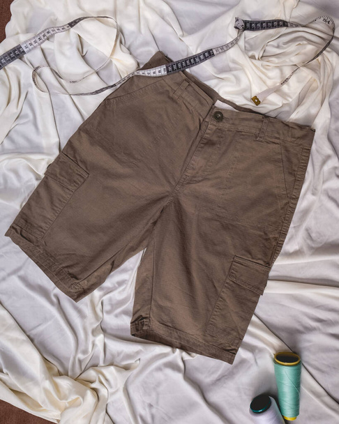 Fashion katoen donker kaki shorts over gerimpeld wit vel met vinyl maat tape en draad kegels - Foto, afbeelding