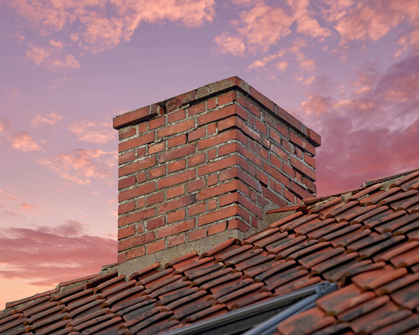 Closeup of red brick chimney against a colorful sunset sky for combustion gases and home insulation on tiled roof. Architecture design on house building for smoke extraction from fireplace or furnace. - Photo, Image