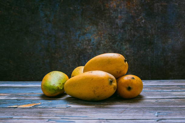 Ryhmä kypsiä mangoja pimeässä ympäristössä puupöydällä. Sivutörmäys. - Valokuva, kuva