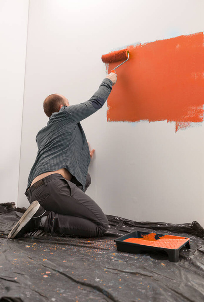 Propriétaire mur de peinture avec peinture orange, wokring sur la rénovation de la maison avec des outils de décoration et pinceau. Redécoration appartement à la maison, peinture manuelle et changement de couleur vibrante. - Photo, image