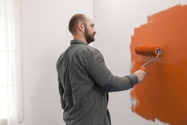 Man renovating apartment with orange paint, using new color on living room wall. Redecorating house with painting tools and paintbrush to change design, home decoration improvement. - Φωτογραφία, εικόνα
