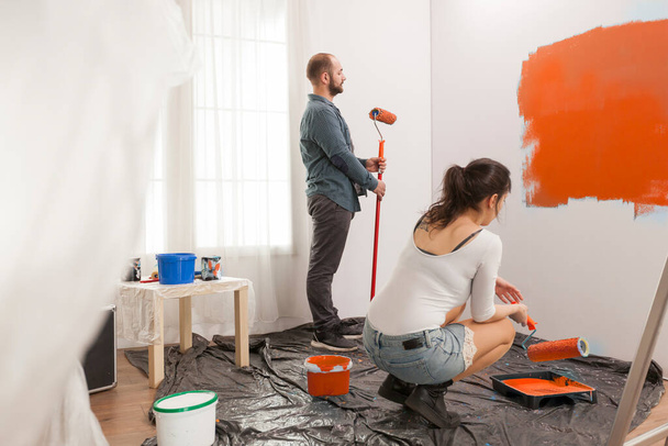 Family painting room with orange color paint to redecorate apartment with paintbrush and roller. Couple doing diy manual renovation using decorating tools and equipment, housework change. - Photo, Image