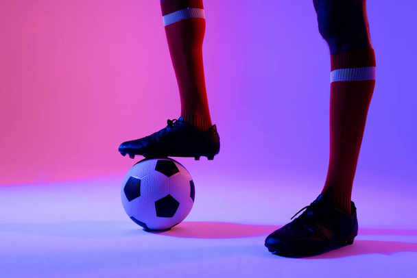 African american male soccer player with football over neon pink lighting. Sport, movement, training and active lifestyle concept. - Foto, imagen
