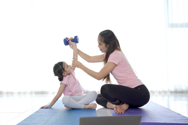 cheerful happy Asian family with father mother and daughter making a home exercise together in the living room. Parent and daughter making a yoga or body stretching exercise. - Photo, image