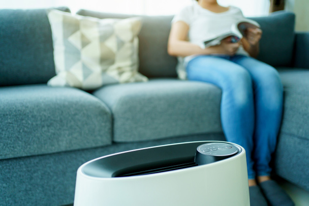 Happy Asian young woman turning on high efficiency air purifier while staying and reading a book in the living room. Woman using air purifier in her house. - Foto, Bild