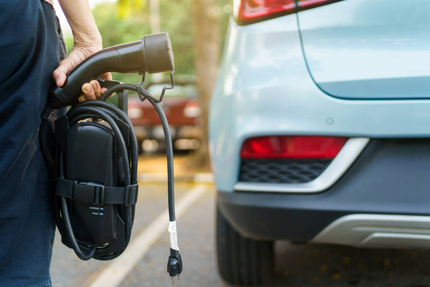 Unrecognizable woman holding the portable EV emergency charging adapter and preparing to charge the EV car. Electric Vehicle charging adapter close up with copyspace. - 写真・画像