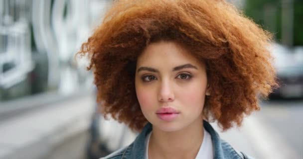 face portrait of a beautiful redhead girl in an urban street. Slow motion of a young calm woman enjoying the fresh air in the city while letting the wind or cool breeze blow through her red afro hair. - Séquence, vidéo