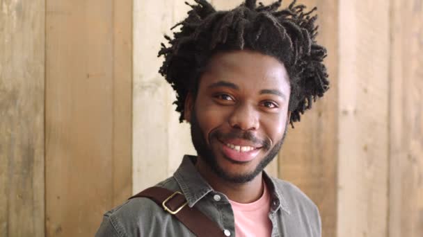 Confident black student or young entrepreneur with a positive and joyful attitude achieving his goals and success. Portrait of happy African man with dreads against a wooden background with copyspace. - Video