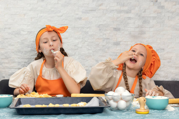 Happy family. Funny girls kids in orange chef uniform are preparing the dough, bake cookies in the kitchen. Sisters children enjoy cooking food. Warm relations. - Foto, imagen