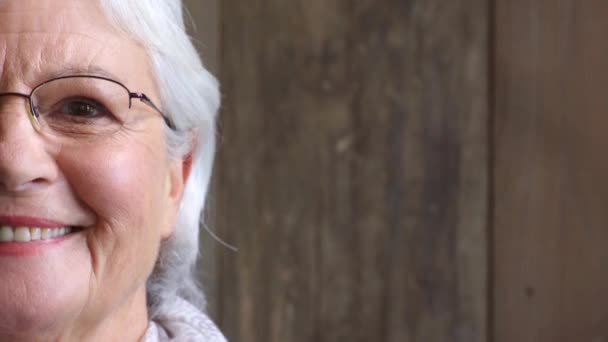 Close-up van een lachende oudere vrouw met voorgeschreven bril voor een beter zicht. Half portret, hoofdfoto en gezicht van een vrolijke, tevreden vrouw met bruine ogen tegen een houten kopieerruimte achtergrond. - Video