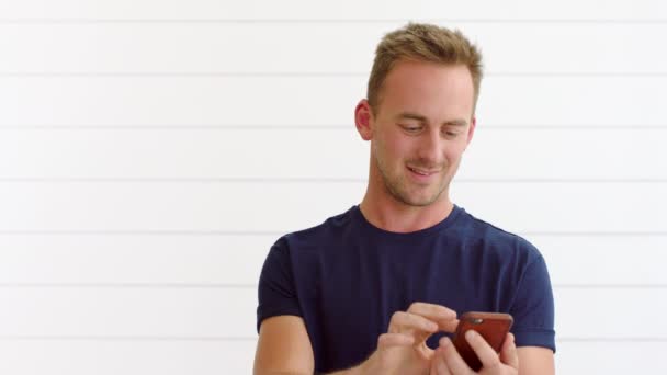 Happy young man using 5g phone against a white background with copyspace. Trendy guy smiling while sending a text, browsing the internet, or using a mobile app and getting good news. - Materiał filmowy, wideo