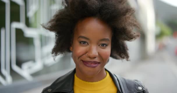 Gezicht van een gespannen jonge vrouw met een afro glimlach. Portret van een mooi trendy zwart meisje dat lacht en haar tanden laat zien. Zelfverzekerde aantrekkelijke Afro-Amerikaanse vrouw met een positieve houding op straat. - Video