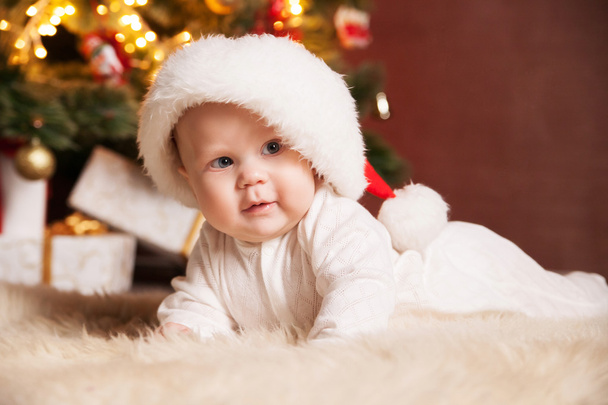 Happy baby wearing Santa hat over christmas tree - Foto, Imagem