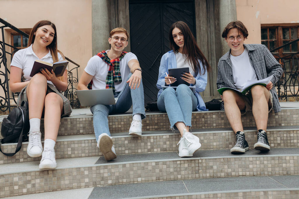 Впевнені студенти. Група щасливих молодих людей, які працюють разом і дивляться на ноутбук, сидячи на сходах
 - Фото, зображення