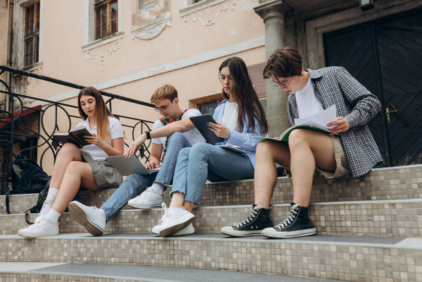 Confident students. Group of happy young people working together and looking at laptop while sitting on steps - Φωτογραφία, εικόνα