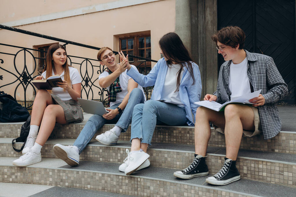 Впевнені студенти. Група щасливих молодих людей, які працюють разом і дивляться на ноутбук, сидячи на сходах
 - Фото, зображення