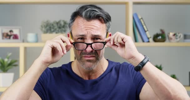 Vidéo 4k d'un bel homme d'âge moyen essayant de voir à travers ses lunettes tout en se tenant à l'intérieur à la maison. - Séquence, vidéo
