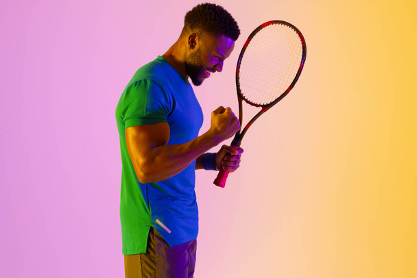 Image of successful african american male tennis player in violet and yellow lighting. Sport, movement, fitness and active lifestyle concept. - Zdjęcie, obraz