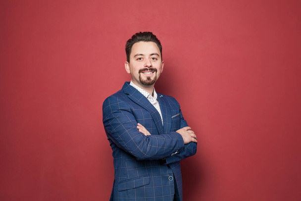 Smiling bearded businessman in blue suit on red background - Фото, зображення