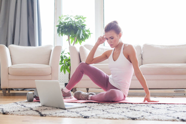 Portrait de jeune femme attrayante apprenant de nouveaux exercices en regardant des tutoriels d'entraînement en ligne sur son ordinateur portable à la maison - Photo, image