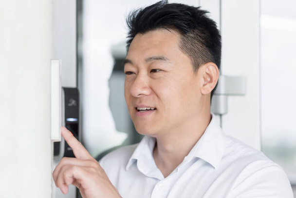 Close-up photo. Portrait of a young handsome Asian man, calling the intercom of the house, pressing the button, waiting for the door to open. - Φωτογραφία, εικόνα