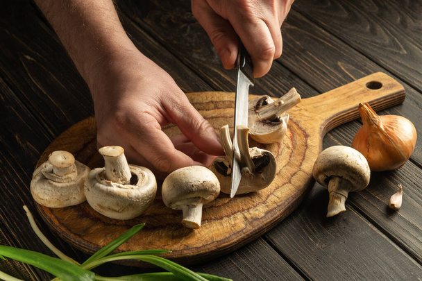 Šéfkuchař krájí houby nožem na dřevěné řezací desce - Fotografie, Obrázek