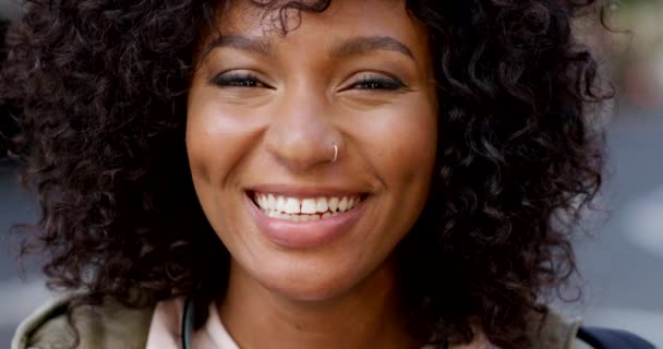 Muotokuva afrikkalaisesta naisesta, jolla on kihara afro hymyilemässä katsellessaan kameraa. Kasvot musta nainen positiivinen asenne ja täydellinen hymy. Edgy ja trendikäs nainen matkustaa kaupunkikaupungissa. - Materiaali, video
