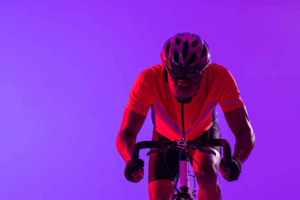 African american male cyclist with bicycle over neon pink lighting. Sport, movement, training and active lifestyle concept. - Photo, image