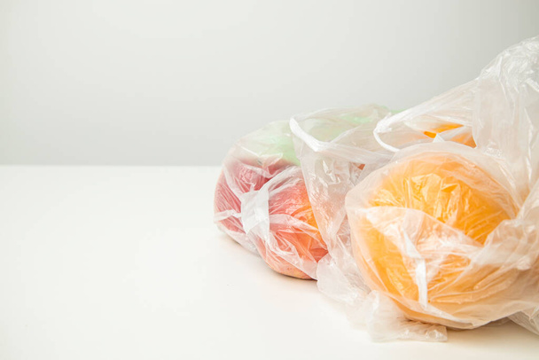 Fresh ripe oranges, apples in transparent plastic bags on a white background. Side view. - Fotó, kép