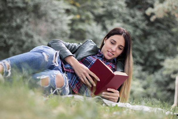 Woman reading a book while laying on the grass. Outdoors, in the park. - Foto, imagen