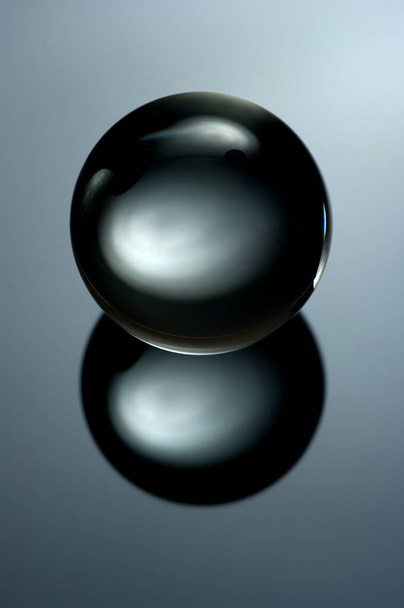 Абстрактное натюрмортное изображение стеклянного шара в низком ключе. Геометрический объект с отражением, Стеклянная сфера в нижней клавише. - Фото, изображение