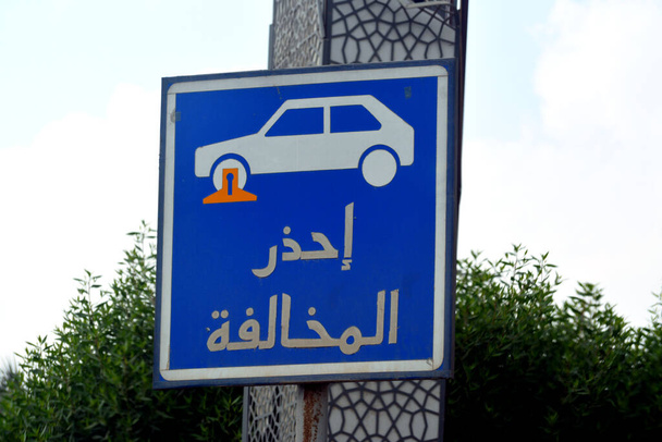 Translation of Arabic inscription (Beware of traffic violation), a traffic sign indicates a restricted area for parking the vehicles and a car with a locked wheel symbol, selective focus - Φωτογραφία, εικόνα