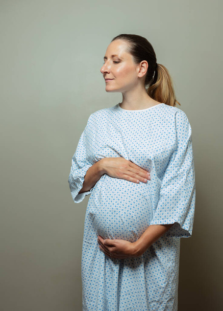Young pregnant woman in hospital robe pose holding big belly tired of complications - Photo, image