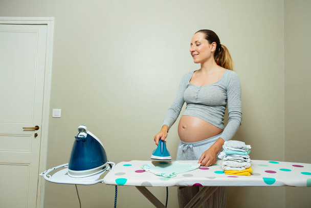 Pregnant woman iron newborn baby clothes preparing for birth of a child - 写真・画像