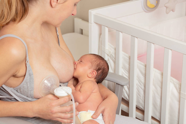 Mother use breast pump and breastfeed newborn baby infant at home in nursery - Фото, изображение