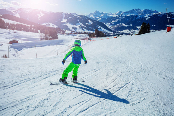 Boy on snowboard move fast downhill on ski alpine sloe from the mountain, rear view - Foto, Bild