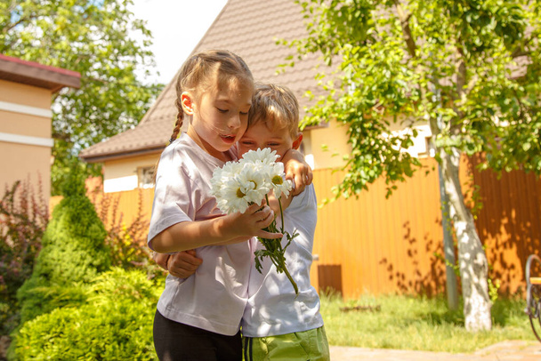 A six-year-old boy gives a girl a bouquet of flowers. Sunny day, in the garden the boy gives a bouquet of daisies to the girl. - Foto, Imagem