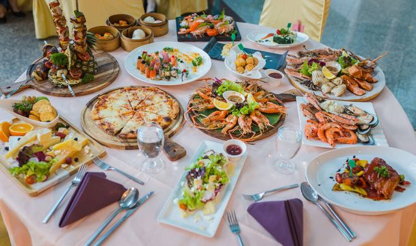 Picture of dinner table set with variety food, seafood, sushi, sashimi, pizza, barbeque, cheese and salad - Foto, imagen