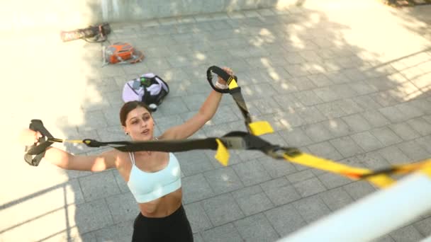 Aantrekkelijke sportieve vrouw die suspensietraining doet met bandjes tijdens een intensieve training in een stedelijke omgeving - Video