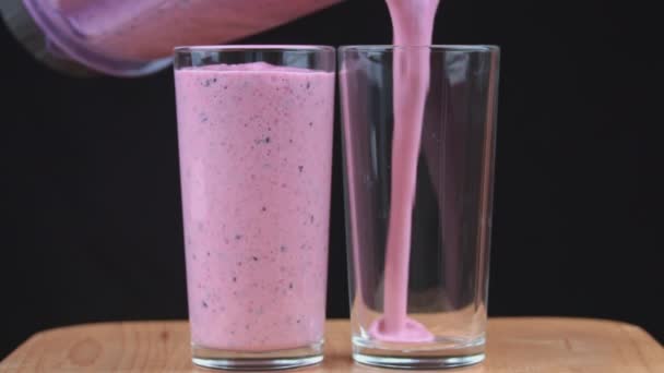 Milkshake with berries is poured into glasses. Two glasses with fresh milkshake. Summer drink with berries and fruits. - Video