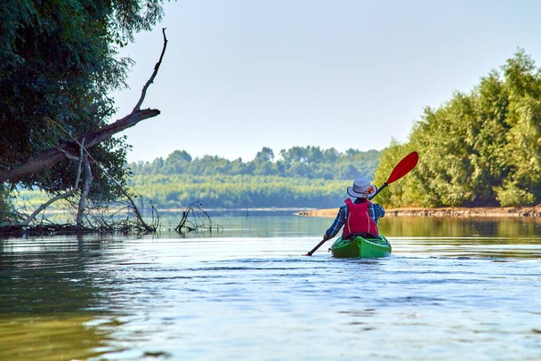 Женщина в элегантной соломенной шляпе канотье греблей зеленый каяк на реке Дунай. Летний водный спорт - Фото, изображение