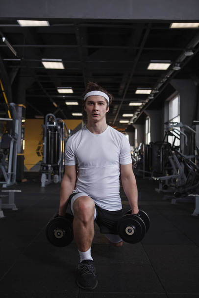 Vertical full length shot of a male athlete doing lunges with dumbbells - Фото, зображення