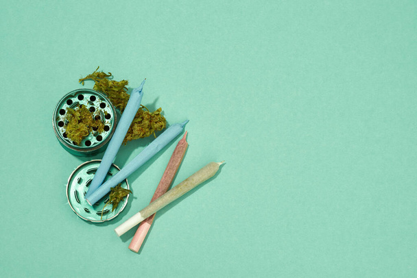 Top view of opened jar with dry marijuana buds and cannabis rolled joints isolated on turquoise background. Light drug and addiction. Herbal medicine. Natural organic cannabis. Copy space - Фото, зображення