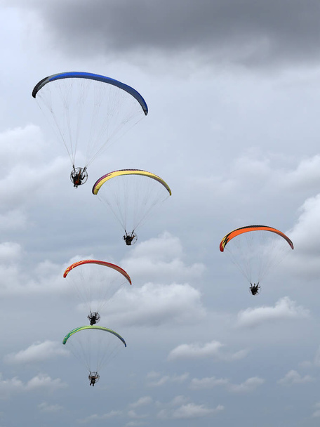 Eine Gruppe bunt motorisierter Gleitschirme fliegt in den blauen Himmel mit Wolken im Hintergrund - Foto, Bild
