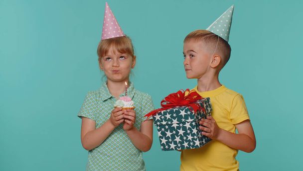 Küçük mutlu çocuklar, erkek ve kız kardeşler ya da doğum günü partisini kutlayan koni şapkalı arkadaşlar, küçük kek kekine mum üfleyip dilek tutuyorlar. Genç anaokulu çocukları - Fotoğraf, Görsel