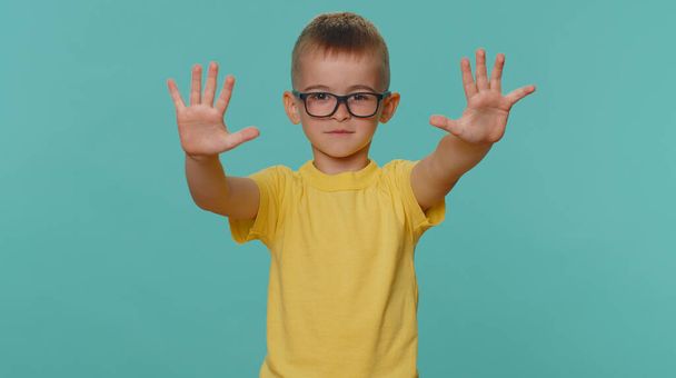 Stop met gebaren. Peuter kinderen jongen zeggen geen handpalm gevouwen gekruiste handen, waarschuwing van afwerking, verboden toegang, afnemende communicatie, lichaamstaal, gevaar. jong kleuter op blauwe achtergrond - Foto, afbeelding
