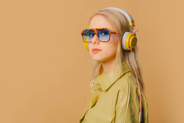 Stylish 80s woman in eyeglasses and headphones on brown background - Zdjęcie, obraz