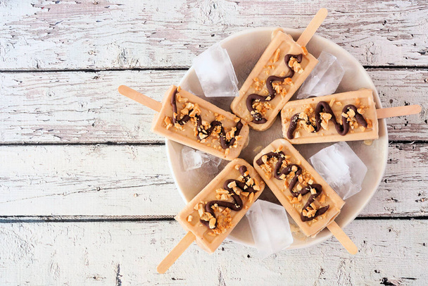 Peanut butter ice pops on a plate. Overhead view on a rustic white wood background. - Photo, Image