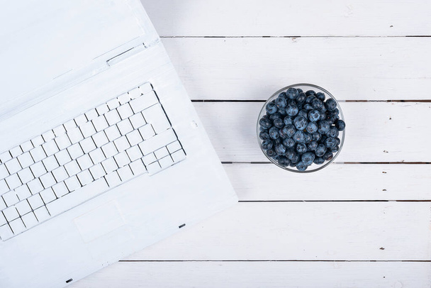 летняя голубая черника на деревянном белом столе с креативно окрашенной тетрадью с белой краской. здоровые идеи для перекуса - Фото, изображение